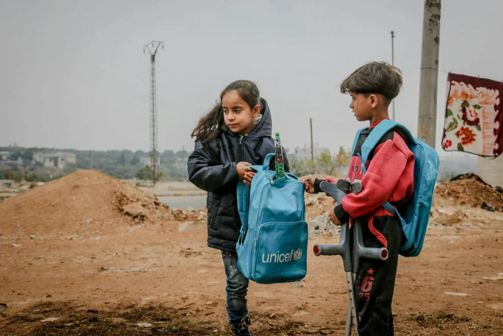 To børn med UNICEF-rygsække står sammen i et område præget af krise og ødelæggelse.